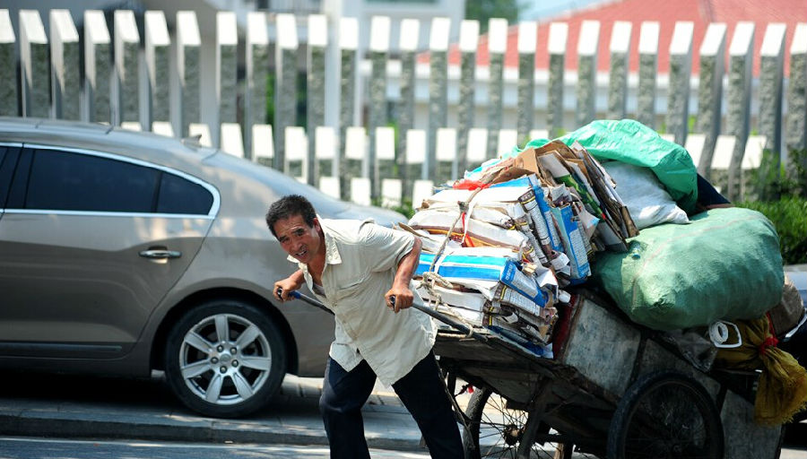 中午12点左右,青岛街头,一名废品回收员吃力地拉车前行.