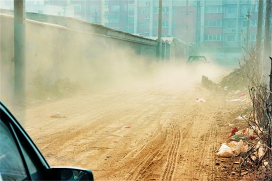 一輛轎車經過,五女冢拆遷現場進出道路上煙塵滾滾.